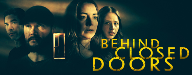 Title card for Lifetime's 2026 film "Behind Closed Doors" featuring Jenny Pudavick as Morgan Marsh, Dennis Andres as Grant, Magalie Langrais as Lizzy Marsh and Chris Hong as Kevin Marsh with serious expressions against a dark, moody background, with a glowing, partially open door positioned between them and the film title in large, distressed yellow typography.