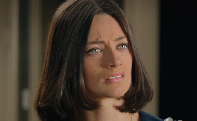 Taylor Anne Danehower as Kelly. A medium close-up of a woman with dark, shoulder-length hair looking slightly to the side with an expression of concern, her eyebrows furrowed and lips slightly parted.
