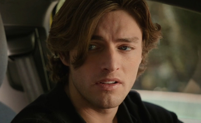 Carson Polish as Sam. A close-up shot of a young man with wavy, shoulder-length light brown hair and blue eyes, looking off to the side with a soft expression while seated inside a vehicle.