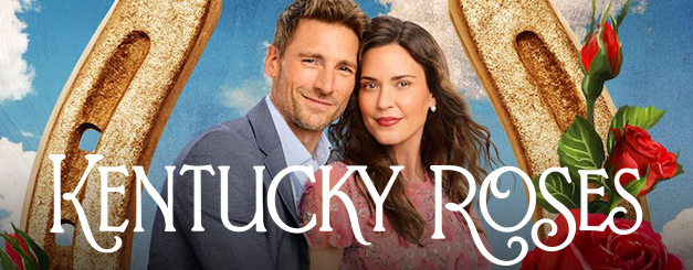 Promotional image for "Kentucky Roses" featuring Andrew Walker as Ash Taylor, a man in a grey suit and Odette Annable as Sadie, a woman in a pink dress standing together. Behind them is a large golden horseshoe against a background of a blue sky with soft clouds. Vibrant red roses with green leaves are positioned in the foreground, and the title "KENTUCKY ROSES" is written in white, elegant lettering across the bottom.