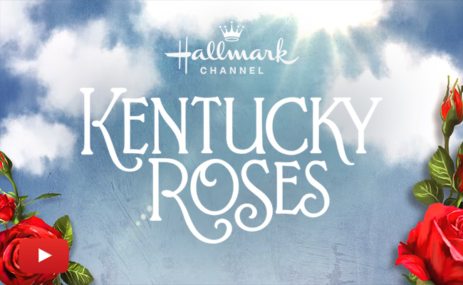 The Hallmark Channel logo appears above the text "Kentucky Roses" in elegant white font, centered against a backdrop of a bright blue sky with soft white clouds. Clusters of vibrant red roses with green leaves frame the bottom left and right corners, and a red YouTube play button icon is positioned in the bottom left.