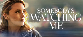 A promotional graphic for "Somebody's Watching Me" featuring Kirsten Comerford as Lori, a woman with highlighted blond hair swept back held by four Bobby pins looking off to the side, set against a dark background with blurred city lights and horizontal light streaks.