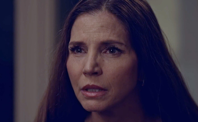 Close-up still of Charisma Carpenter as Rena, a woman with long dark hair, looking off-camera with an earnest and concerned expression.