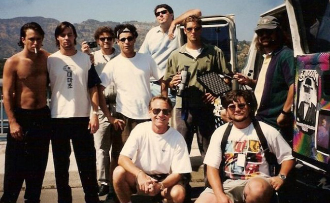 Publicity still for MTV's "Buzzkill", featuring the cast and crew, a group of men including series stars Travis Draft, Dave Sheridan, Frank Hudetz and Vince D'Orazi, posing in front of a van with a psychedelic mural, mountains in the background.